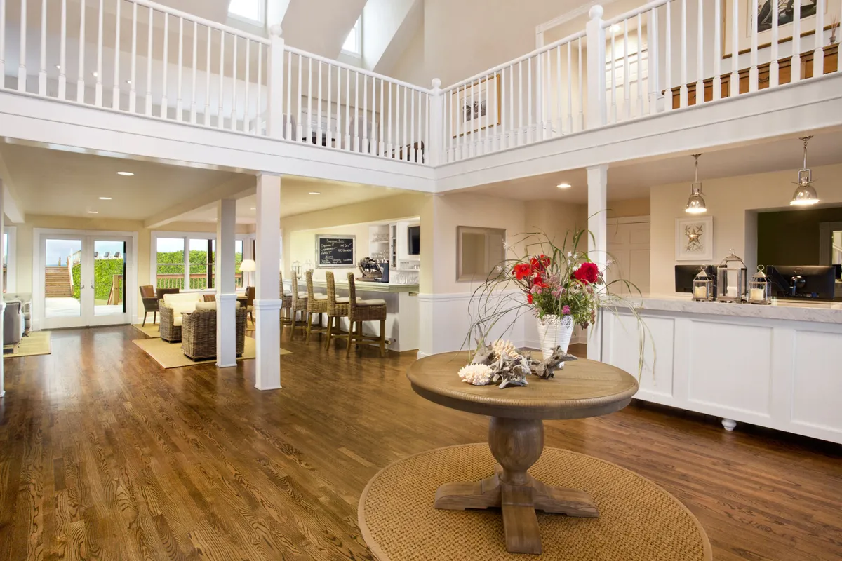 A bright, open living space featuring a central round table adorned with a floral arrangement. High ceilings and expansive windows fill the room with natural light, while comfortable seating invites guests to linger. The room is designed to facilitate gatherings and entertaining, with views that enhance the atmosphere.