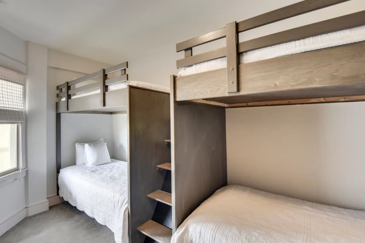 A cozy bunk room with neatly made white bedding and sturdy wooden furniture. The space is welcoming and bright, ideal for kids or groups of friends seeking a fun, shared sleepover experience.