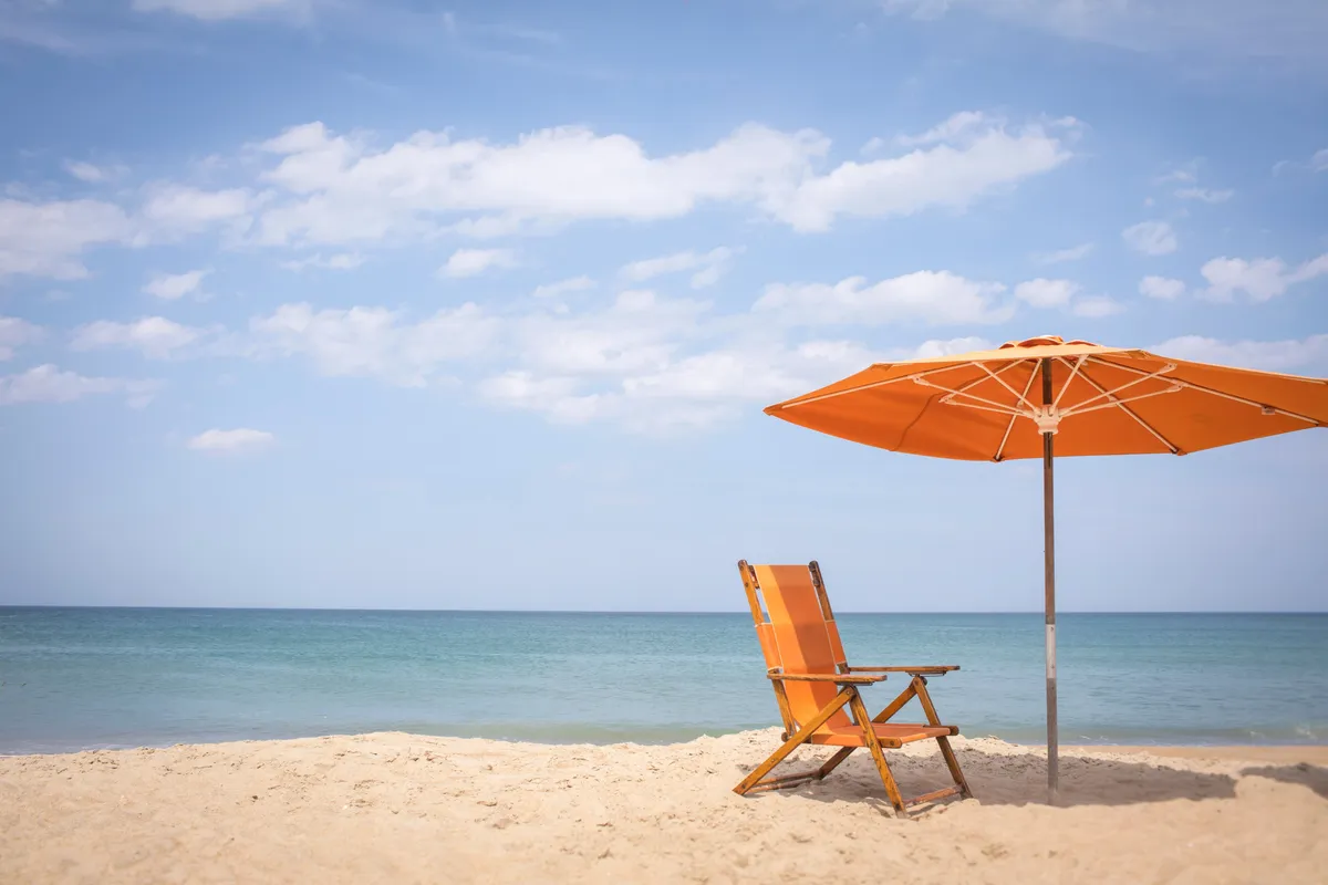 A peaceful beach scene with a single lounge chair and umbrella set on soft sand, overlooking the ocean. The atmosphere is quiet and reflective, perfect for sunbathing, reading, or unwinding by the water.