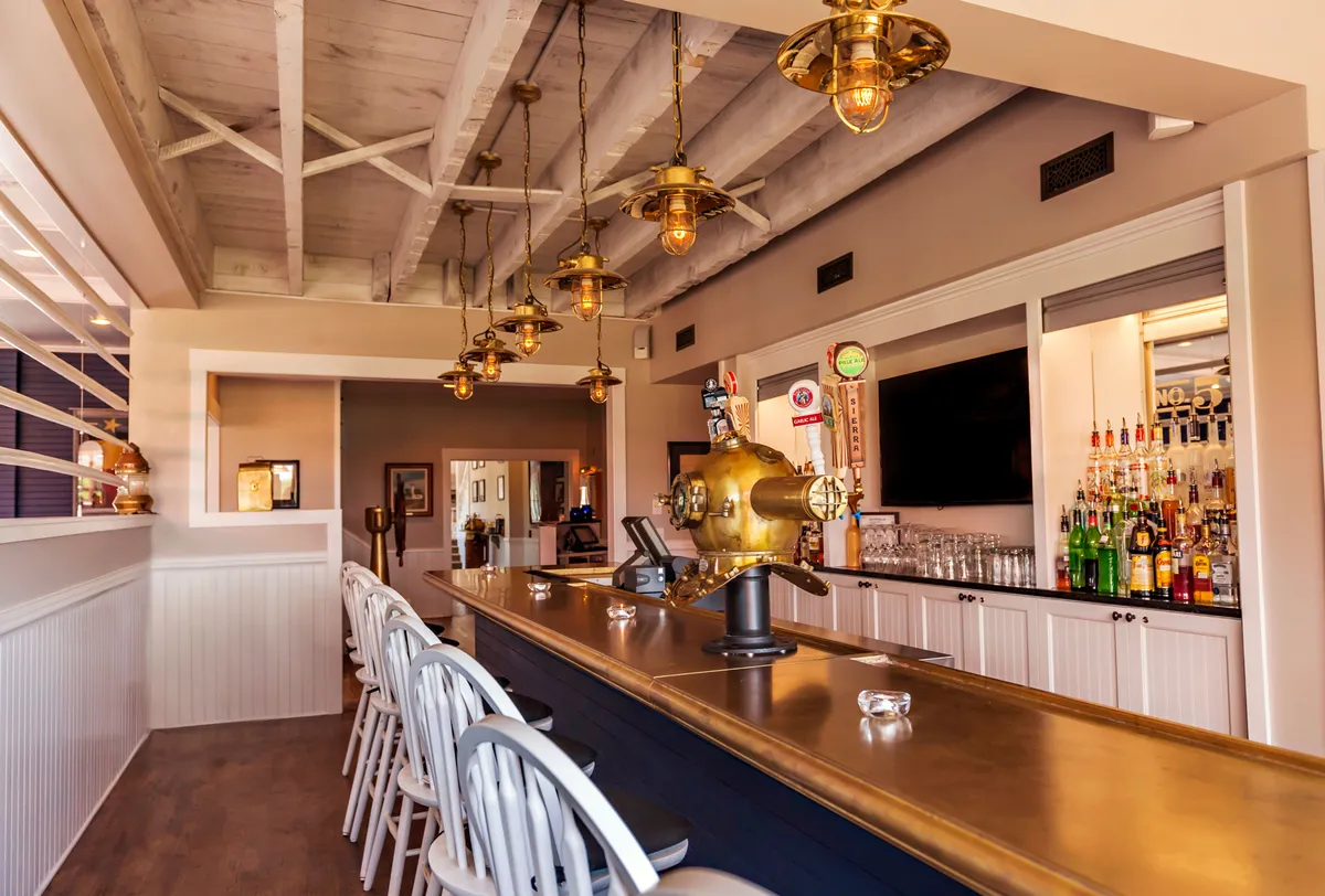 A stylish bar counter with hanging lights and shelves lined with bottled drinks. The atmosphere is cheerful, making the space ideal for relaxed coffee chats or gathering before or after meals.