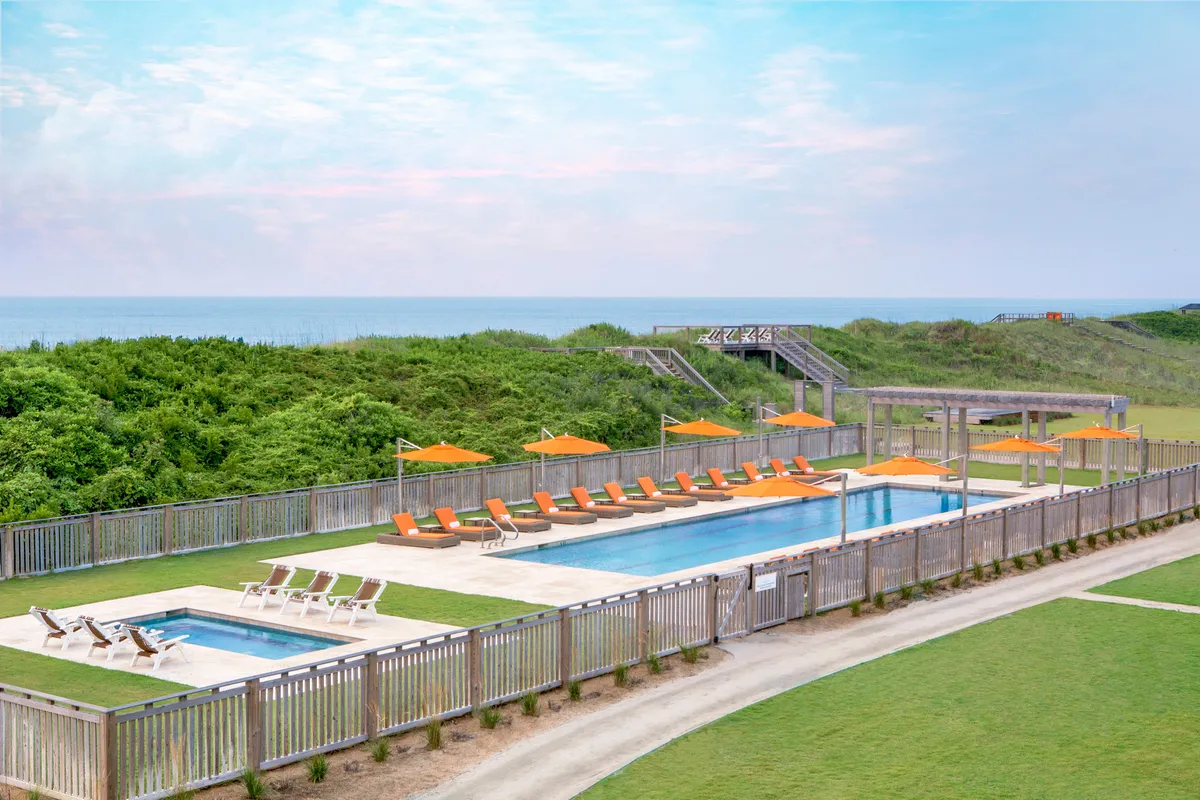 A sun-drenched pool area featuring inviting lounge chairs, vibrant orange umbrellas, and lush greenery. The tranquil setting is perfect for sunbathing, relaxing after a spa day, or early morning yoga sessions.